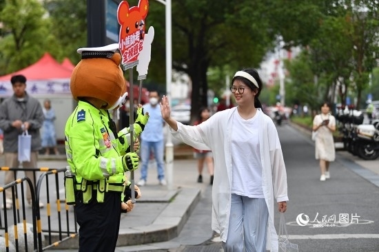 6月7日上午9時(shí)，隨著鈴聲的響起，2023年江西高考正式開考，江西省的53.57萬考生以縣（區(qū)）為單位隨機(jī)安排在全省256個(gè)考點(diǎn)、18968個(gè)考場(chǎng)參加高考。圖為“小熊交警”和考生擊掌鼓勵(lì)。 人民網(wǎng)記者 時(shí)雨攝