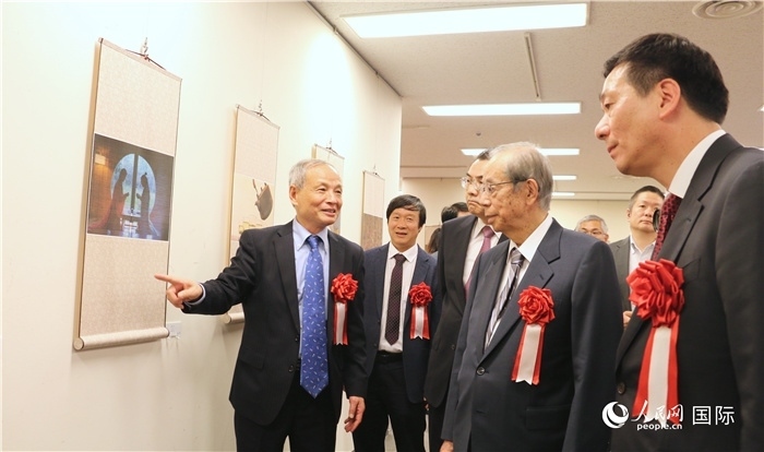 “湖州印象”攝影展主創(chuàng)、世界華人攝影協(xié)會副會長馮學(xué)敏向吳江浩大使、福田康夫前首相等嘉賓介紹展出作品。（人民網(wǎng) 許可攝）