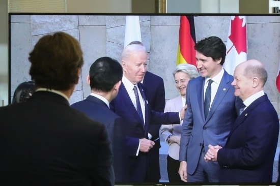 2022年3月24日，在比利時(shí)布魯塞爾的北約總部，一名男子觀看屏幕上美國(guó)總統(tǒng)拜登（右四）、歐盟委員會(huì)主席馮德萊恩（右三）、加拿大總理特魯多（右二）、德國(guó)總理朔爾茨（右一）出席七國(guó)集團(tuán)峰會(huì)合影儀式的畫(huà)面。新華社記者鄭煥松攝