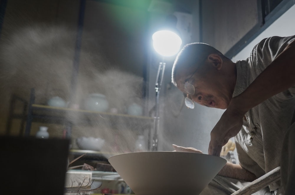 ↑ 在景德鎮(zhèn)，手工匠人吹去坯內(nèi)的泥土（2021年7月14日攝）。