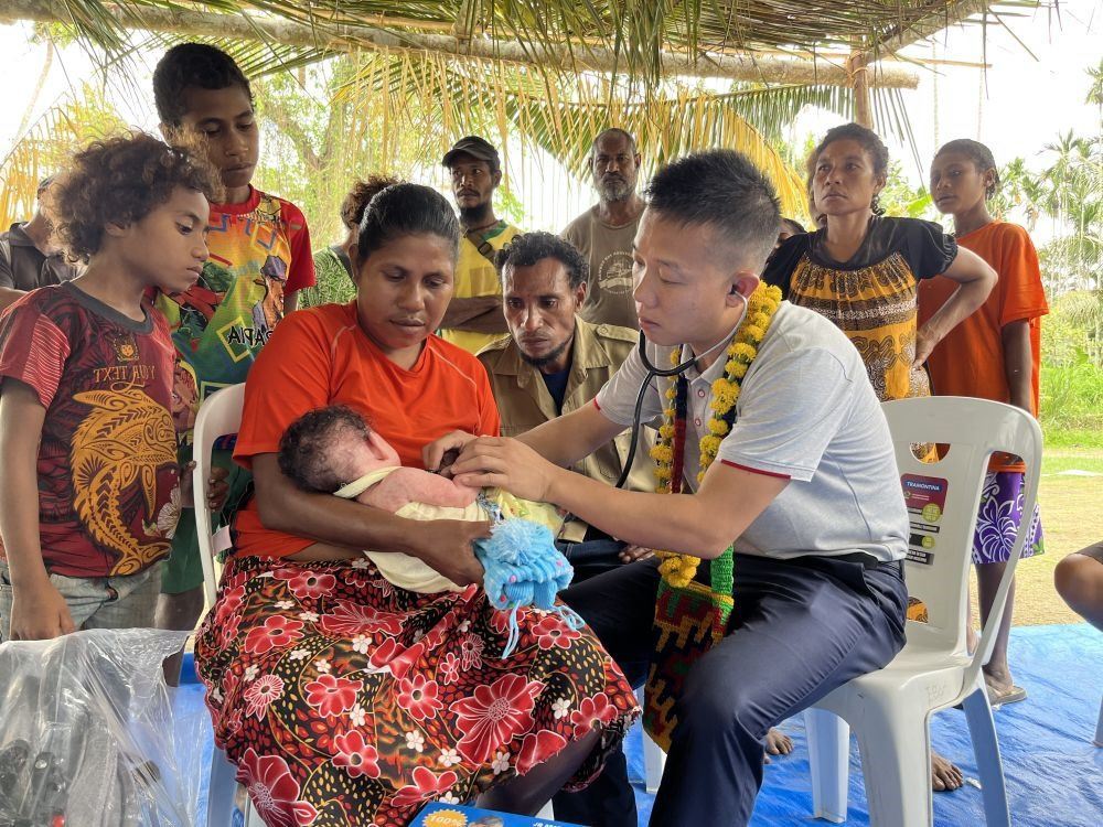 2023年8月5日，在巴布亞新幾內(nèi)亞中央省的一個(gè)村莊里，第12批援巴新中國醫(yī)療隊(duì)副隊(duì)長、新生兒科副主任醫(yī)師劉振球?yàn)閶雰禾仿犜\檢查。泰樂出生時(shí)患有重癥，一度生命垂危，經(jīng)過劉振球與當(dāng)?shù)蒯t(yī)護(hù)人員的救治最終痊愈。從2002年起，中國連續(xù)向巴新派出12批醫(yī)療隊(duì)，為提高巴新醫(yī)療衛(wèi)生水平作出積極貢獻(xiàn)。