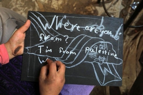 2023年12月28日，一名學生在加沙地帶南部城市拉法一所學校的臨時教室中寫下“我來自巴勒斯坦”的字樣。新華社發(fā)（里澤克·阿卜杜勒賈瓦德攝）