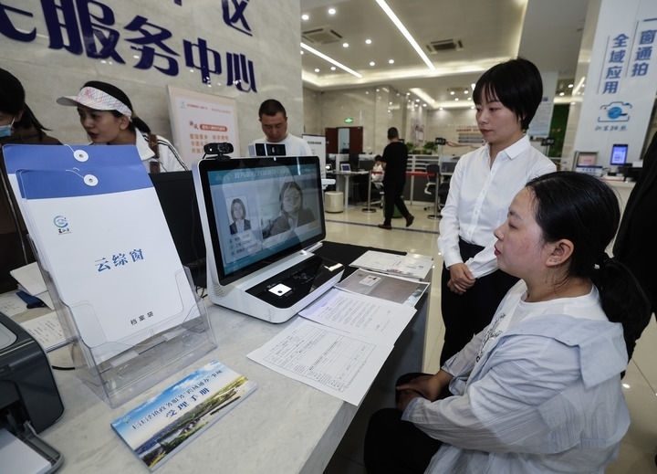 在浙江省嘉興市秀洲區(qū)王江涇鎮(zhèn)便民服務(wù)中心的“跨域通辦·云綜窗”窗口，辦理開業(yè)登記的個體工商戶（右一）通過該系統(tǒng)與江蘇省蘇州市吳江區(qū)盛澤鎮(zhèn)行政審批局工作人員視頻連線，進行身份讀取及材料線上審核（2024年5月9日攝）。新華社記者 徐昱 攝