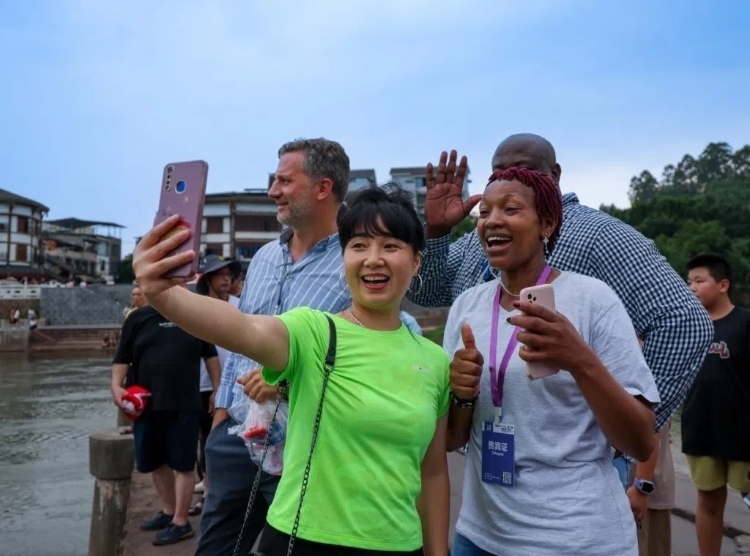 2024“一帶一路”媒體合作論壇聯(lián)合采訪調(diào)研行成員在樂山蘇稽古鎮(zhèn)與游客合影留念。本報(bào)記者 伊霄攝