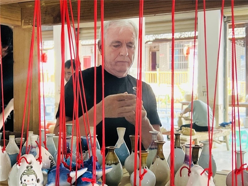 鄉(xiāng)愁如同一根根紅線，將游子與故鄉(xiāng)永遠(yuǎn)地牽連到一起?；逄账囄幕瘎?chuàng)意一條街的母氏陶藝館內(nèi)，紅線吊著陶瓶，思緒游走萬里。摩爾多瓦“信息標(biāo)簽”通訊社社長(zhǎng)亞歷山大·塔納斯端詳著館內(nèi)展示的陶藝作品，并挑選出心儀的小擺件帶回摩爾多瓦，也帶走花茂村的“鄉(xiāng)愁”。（張亞欣攝）